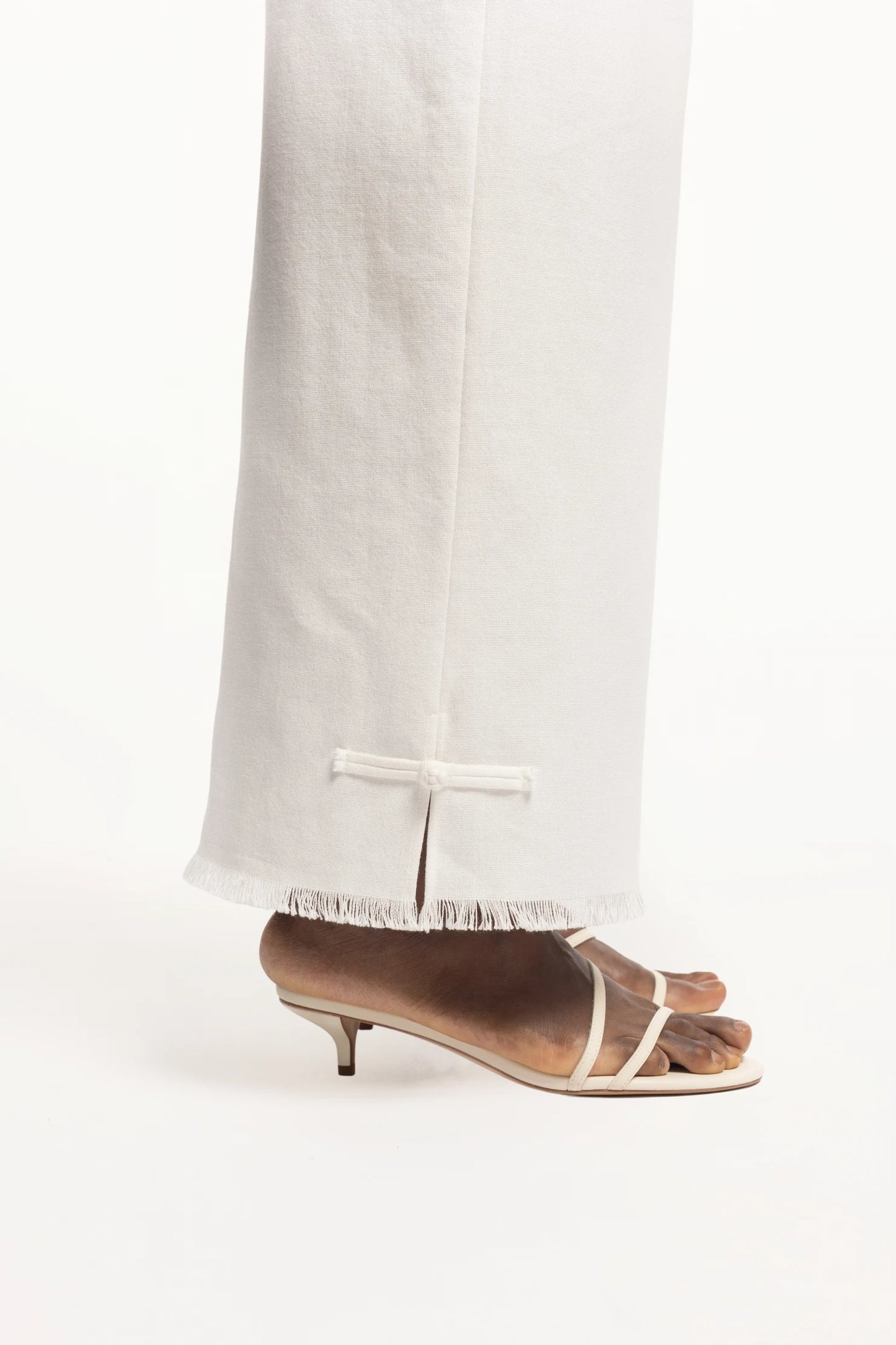 Cruise Trousers | MAISON MAGDALNEA | White cotton trousers with a handmade frog button as decoration at the bottom | Close up picture of the model's feet