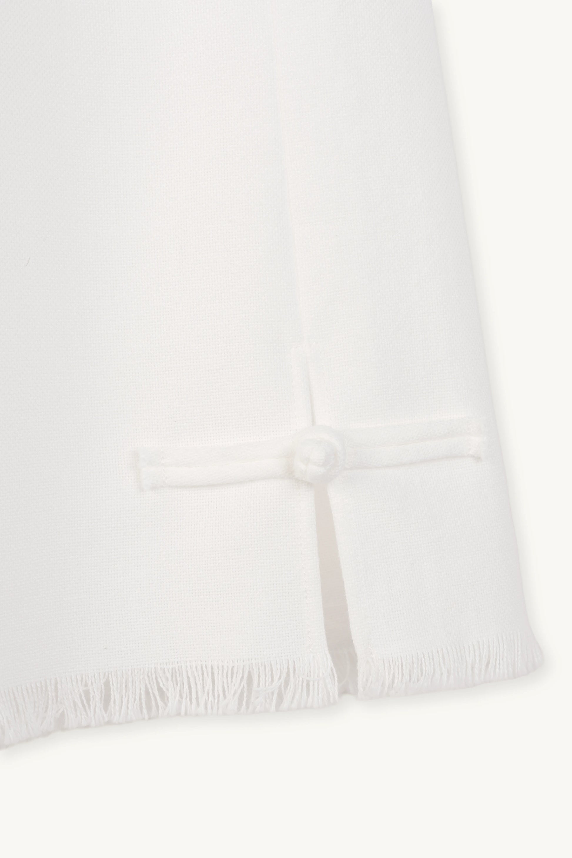 Cruise Trousers | MAISON MAGDALNEA | White cotton trousers with a handmade frog button as decoration at the bottom | close up picture of the button on light background