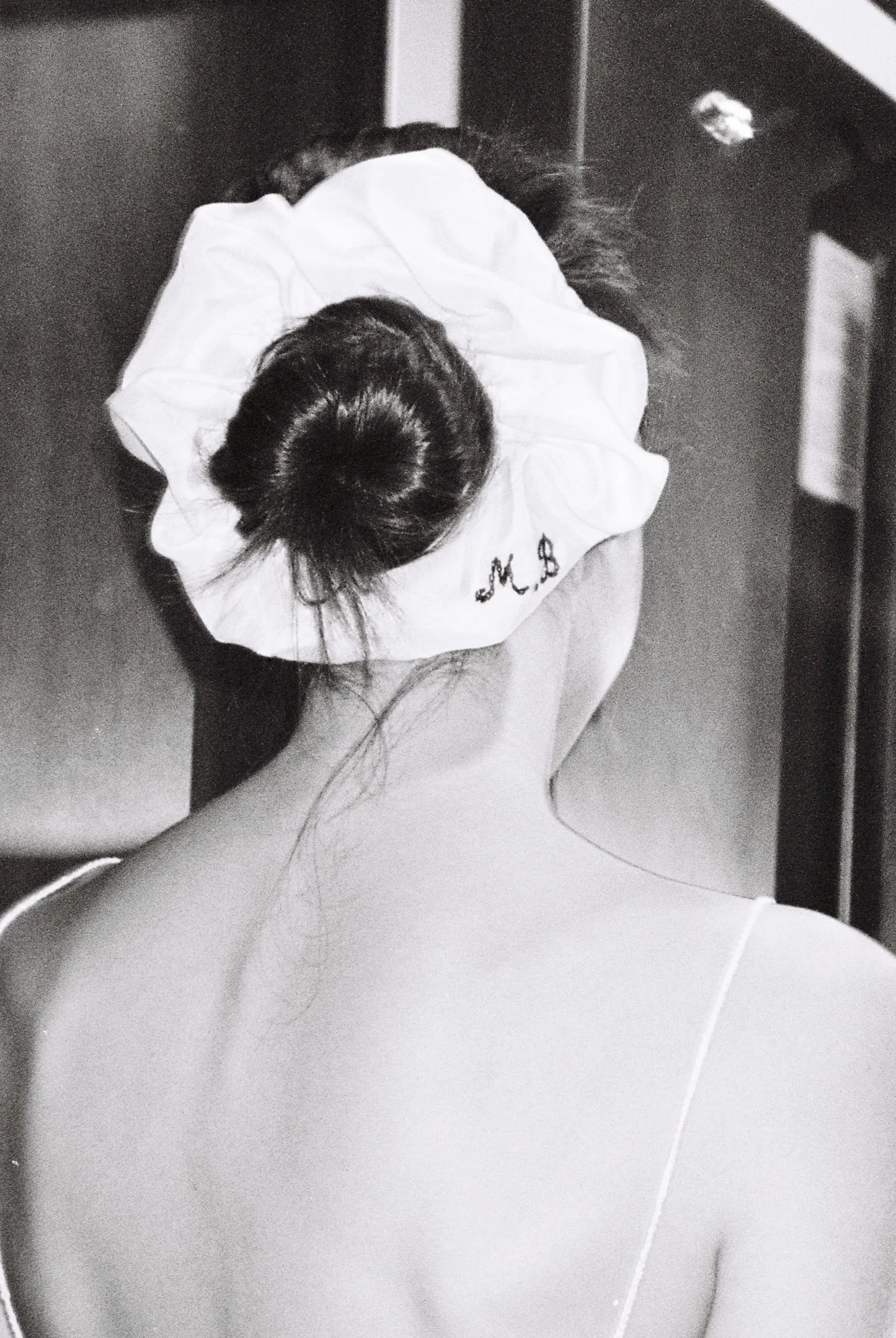 Person with a white MAISON MAGDALENA silk scrunchie featuring her initials, viewed from behind.