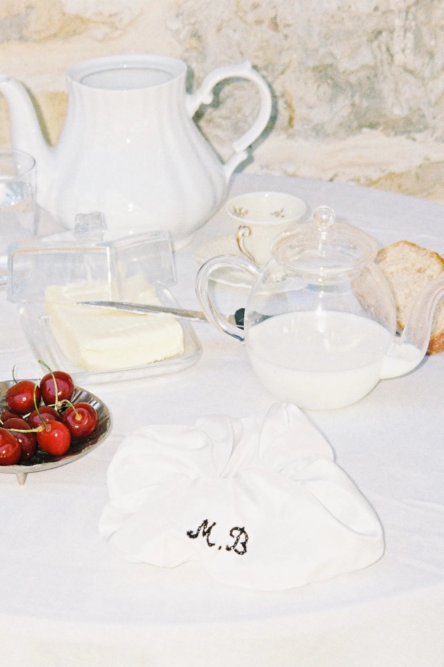MAISON MAGDALENA | ANTIPASTI SCRUNCHIE with embroidered initials placed on a garden table next to ceramic tablewear