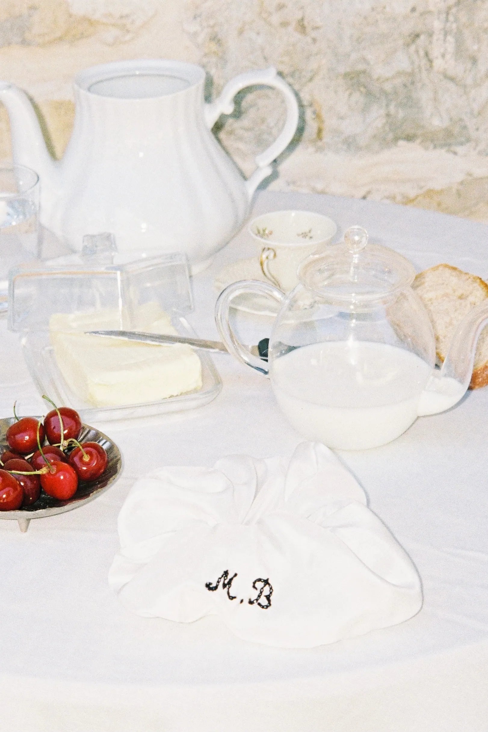 MAISON MAGDALENA | ANTIPASTI SCRUNCHIE with embroidered initials placed on a garden table next to ceramic tablewear